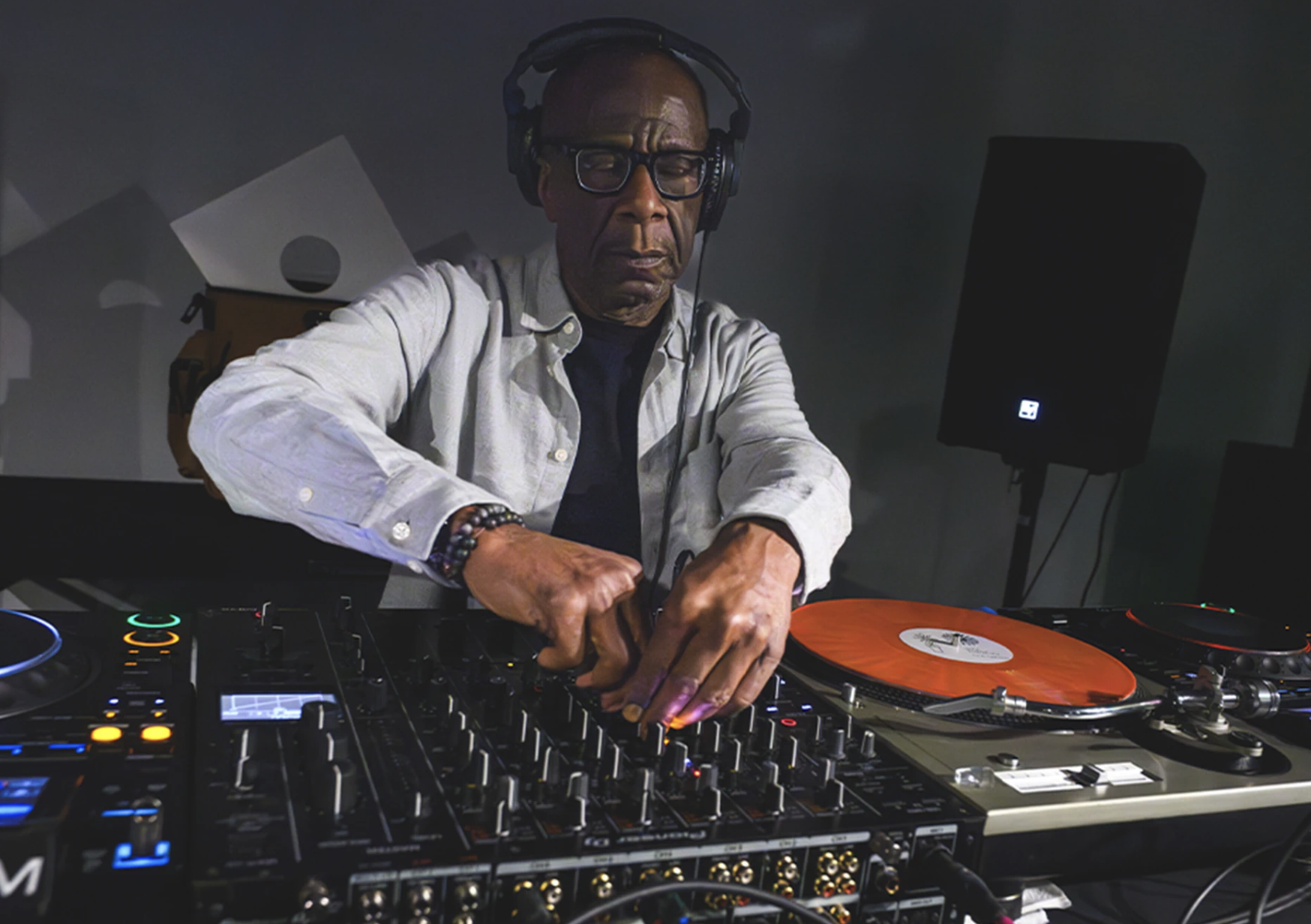 DJ John Collins wearing headphones mixes music behind a sound mixing board.